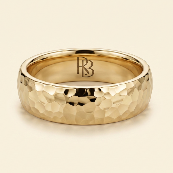 A gold band mens wedding ring with a hammered texture on the exterior and a polished interior by ring bear with comfort fit, set against a solid cream background.