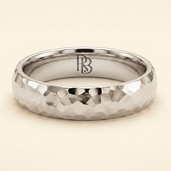 A white gold band mens wedding ring with a hammered texture on the exterior and a polished interior by ring bear with comfort fit, set against a solid cream background.