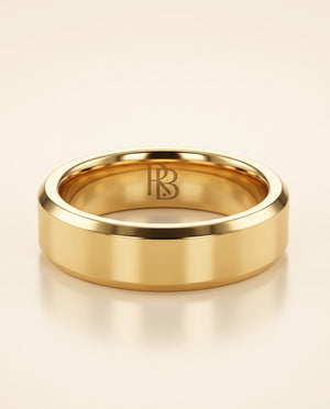 A polished yellow gold  beveled tungsten band ring with a polished finish and an engraved 'RB' monogram inside, displayed on a warm cream background.