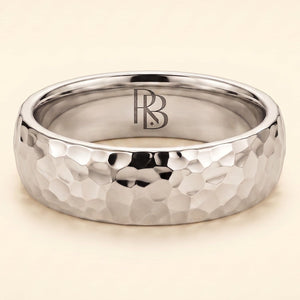 A white gold band mens wedding ring with a hammered texture on the exterior and a polished interior by ring bear with comfort fit, set against a solid cream background.