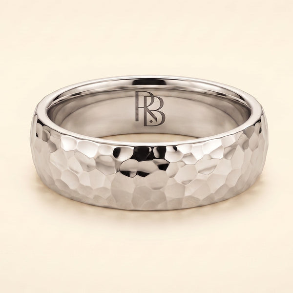 A white gold band mens wedding ring with a hammered texture on the exterior and a polished interior by ring bear with comfort fit, set against a solid cream background.