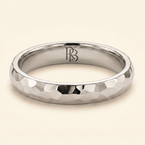 A white gold band mens wedding ring with a hammered texture on the exterior and a polished interior by ring bear with comfort fit, set against a solid cream background.
