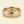 A gold band mens wedding ring with a hammered texture on the exterior and a polished interior by ring bear with comfort fit, set against a solid cream background.