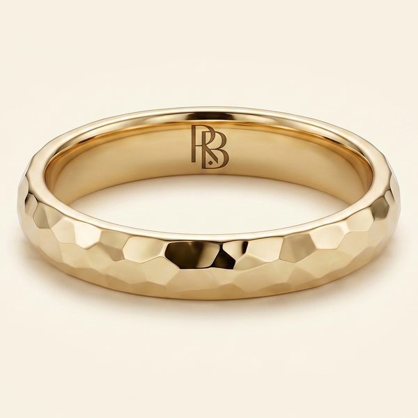 A gold band mens wedding ring with a hammered texture on the exterior and a polished interior by ring bear with comfort fit, set against a solid cream background.