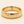 A yellow gold band mens wedding ring with a hammered texture on the exterior and a polished interior by ring bear with comfort fit, set against a solid cream background.