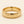 A yellow gold band mens wedding ring with a hammered texture on the exterior and a polished interior by ring bear with comfort fit, set against a solid cream background.